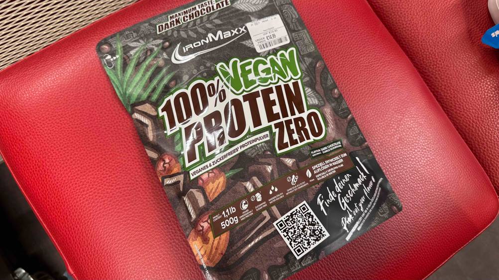 Auf einem roten Polster liegt eine Packung des getesteten Schoko-Proteinpulvers.