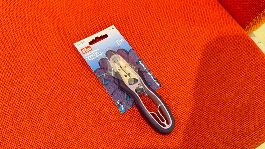 Detailansicht von oben einer Fadenschere, die zum testen im Kartonblister auf einer orangenen Fläche liegt.