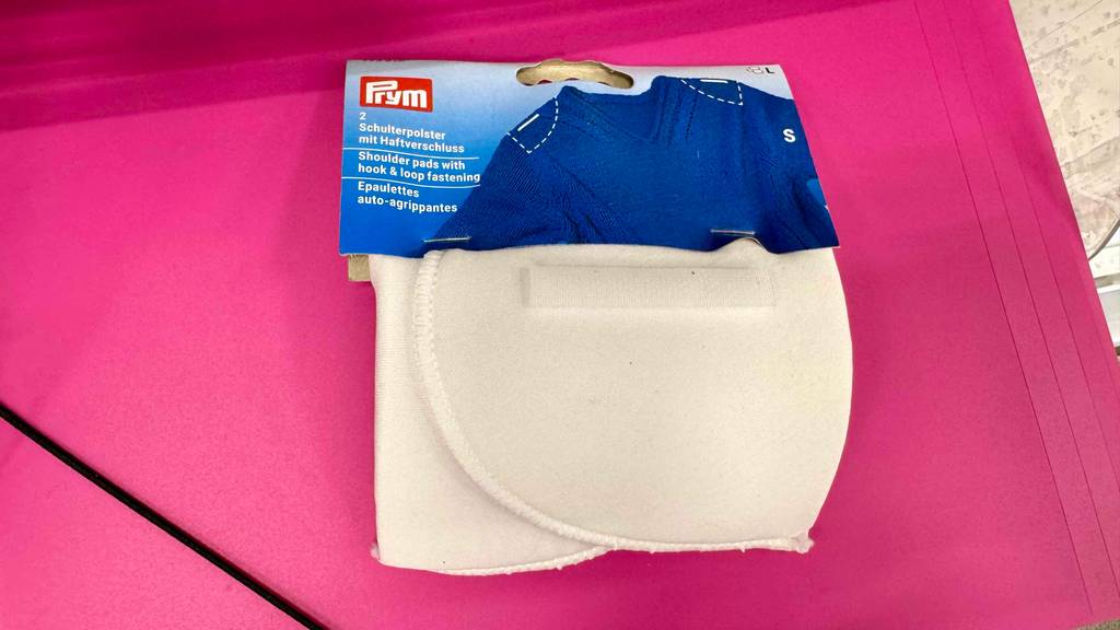 Getestetes Schulterpolster liegt im Blister auf einer rosa Fläche.