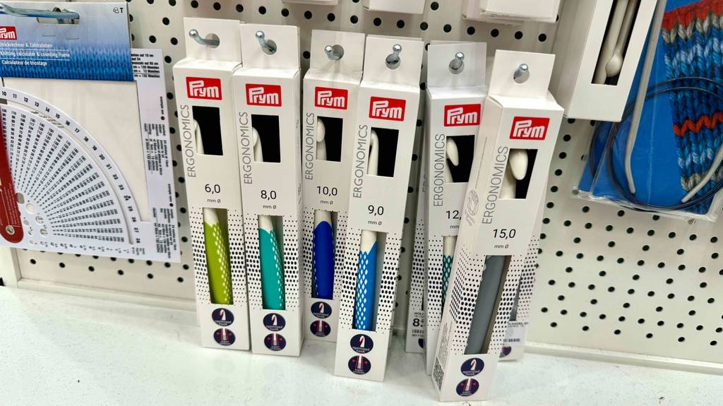 Unterschiedlich große tunesische Häkelnadeln im Test befinden sich in ihren Verpackungen an einem Verkaufsregal.