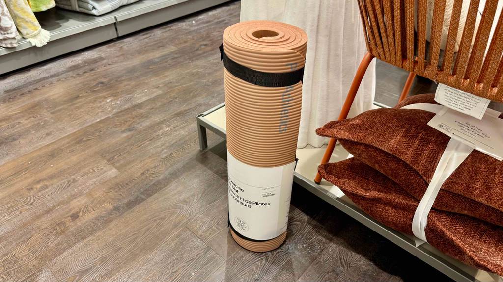 Eine Yogamatte XL steht zum testen in einem großen Raum vor einem Regal mit Kissen.