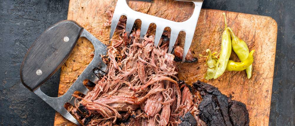 Pulled-Pork-Krallen-Test: Fleisch auf einem Holzbrett, neben zwei Fleischkrallen und Peperoni