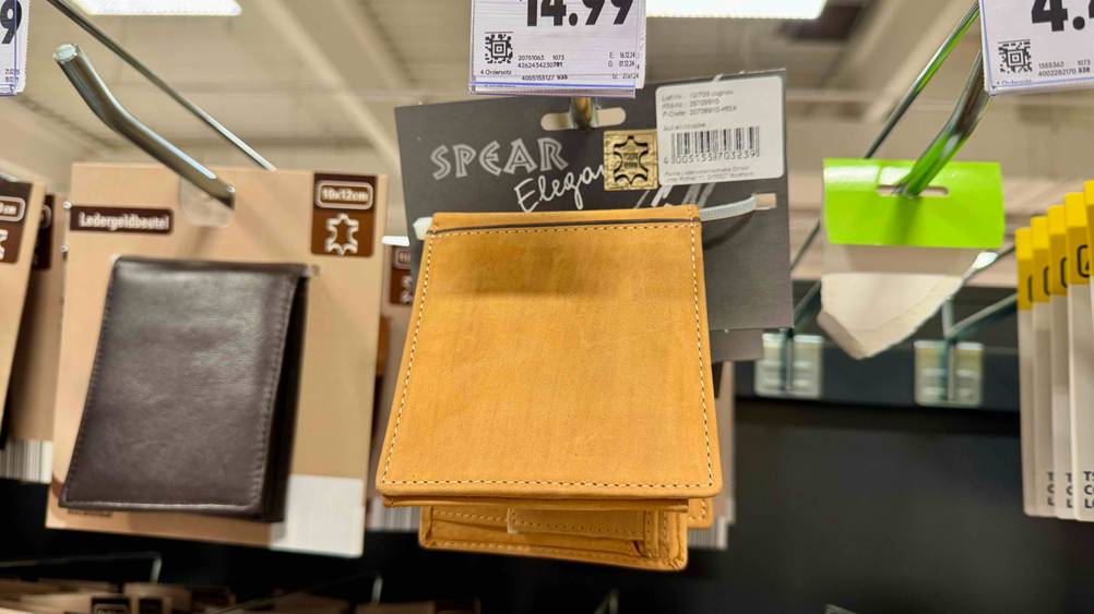 Eine getestete Unisex-Geldbörse aus echtem Leder hängt neben weiteren Geldbörsen an einem Verkaufsstand.