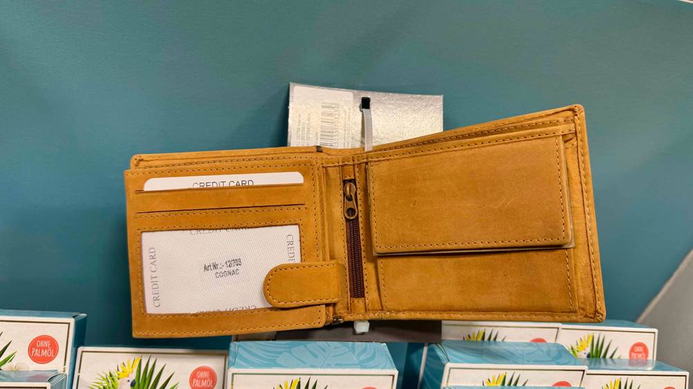 Eine geöffnete getestete Unisex-Geldbörse mit diversen Fächern liegt auf mehreren Kartons.