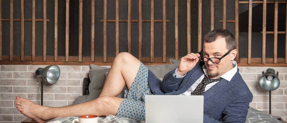 puma-boxershorts-test: Mann in Boxershorts und Anzugjacke liegt auf Bett und arbeitet am Laptop.