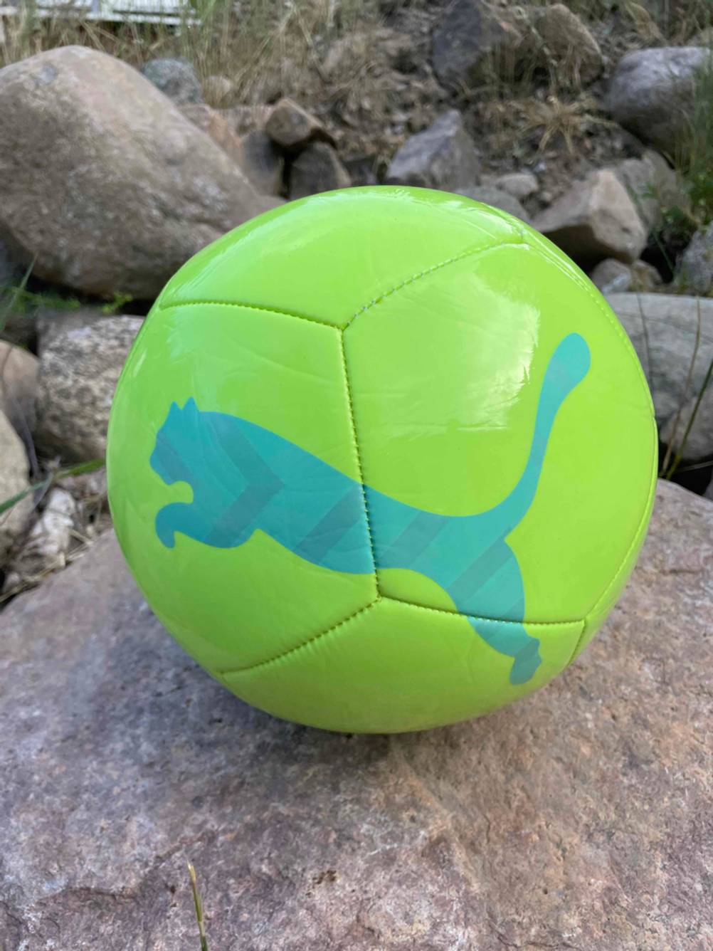 Ein gelber Fussball mit Pumaaufdruck liegt getestet auf großen Steinen.
