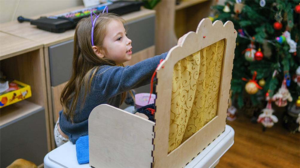 Puppentheater im Test: Ein kleines Mädchen spielt vor einem Weihnachtsbaum mit einem Tisch-Puppentheater.