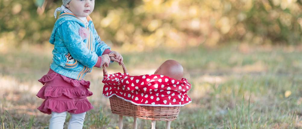 mädchen mit puppenwagen aus holz auf gras