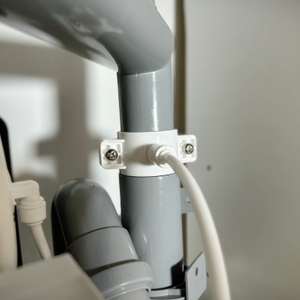 Ein weißer Schlauch der Osmoseanlage ist mit einer Schelle an ein graues Abflussrohr unter der Spüle angeschlossen. Die Verbindung ist mit zwei Schrauben gesichert.