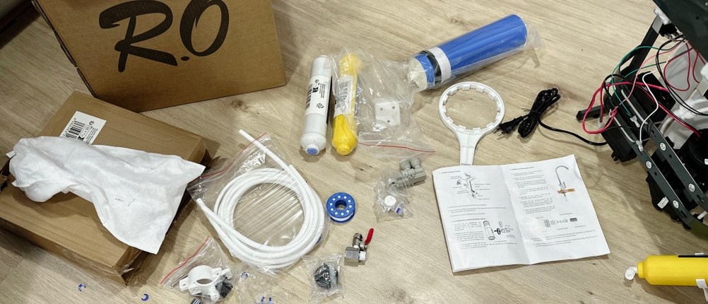 Ein geöffneter Karton zeigt den gesamten Lieferumfang der Osmoseanlage. Sichtbar sind Filter, Schläuche, Zubehörteile und eine Anleitung.