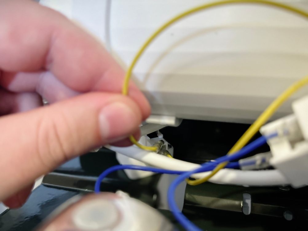 Ein gelbes Kabel wird von einer Hand gehalten und vor einem weißen Anschluss gezeigt. Das Kabel ist nicht eingesteckt.