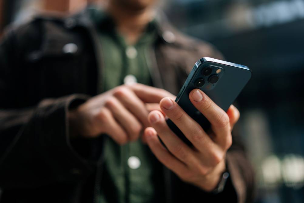 Ein Mann hält unterwegs sein Smartphone in der Hand und tippt.
