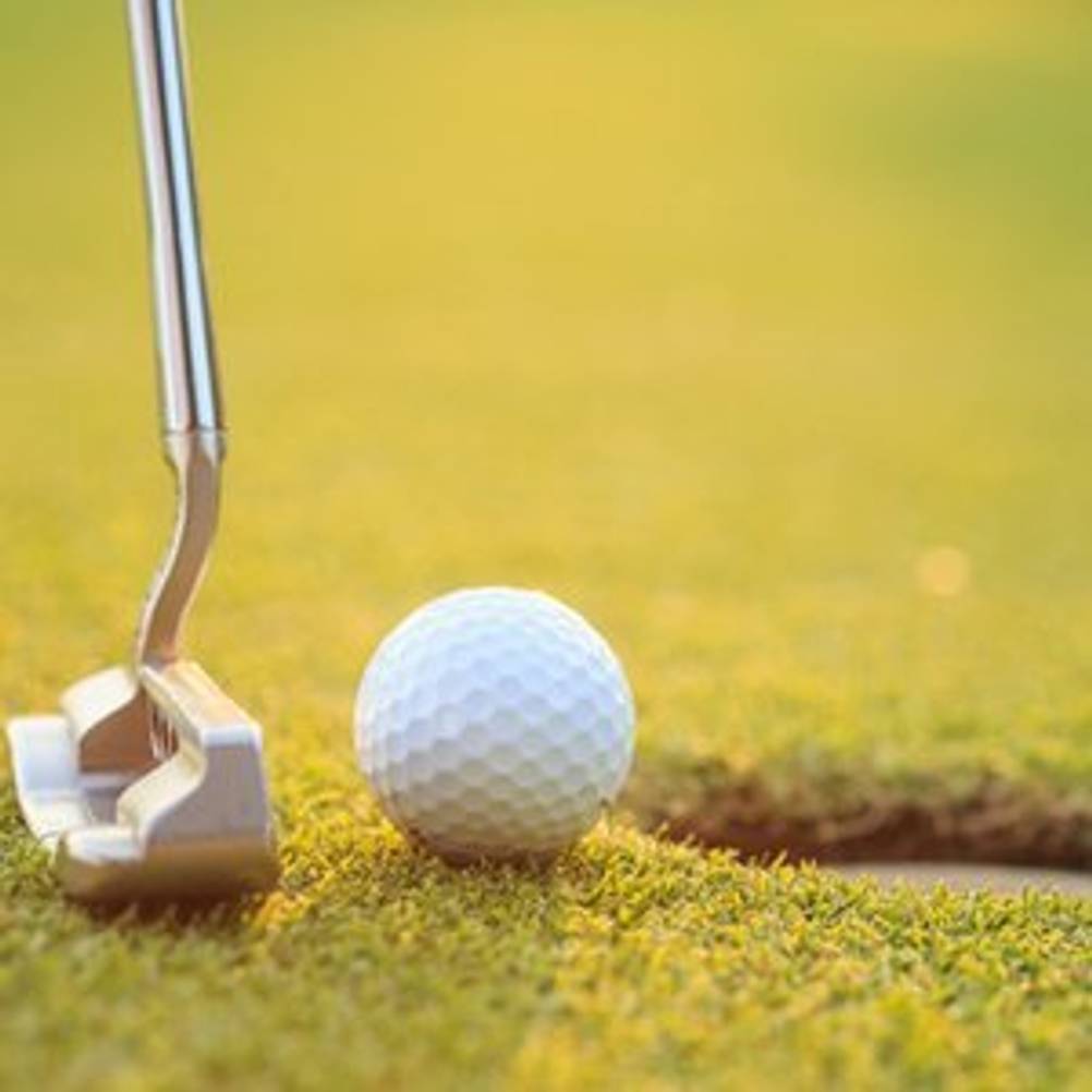 Putter und Golfball wenige Millimeter entfernt von einem Loch