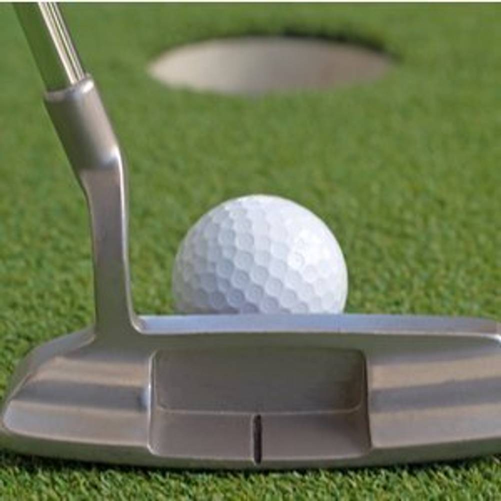 Putter, der einen Golfball vor einem Loch anvisiert