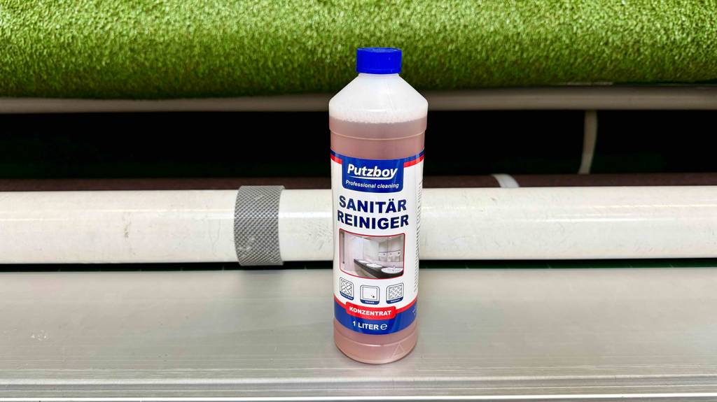 Der getestete Sanitärreiniger in der 1-Liter-Kunststoffflasche steht auf einem weißen Regal.