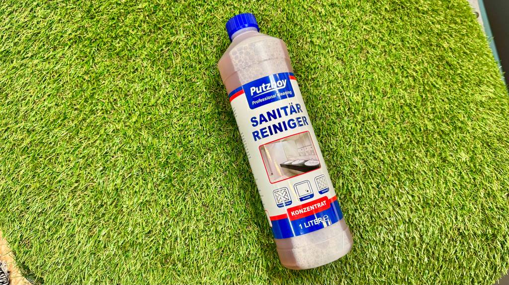 Der Sanitärreiniger im Test liegt innerhalb einer 1-Liter-Kunststoffflasche auf einem grünen Kunststoffrasen.