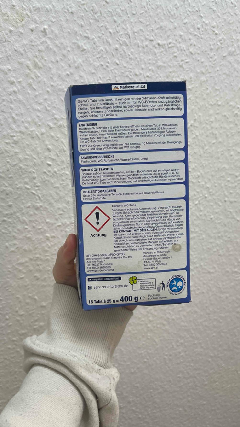 Eine Hand hält die Rückseite der getesteten Putzmittel-Tabs vor eine Wand.