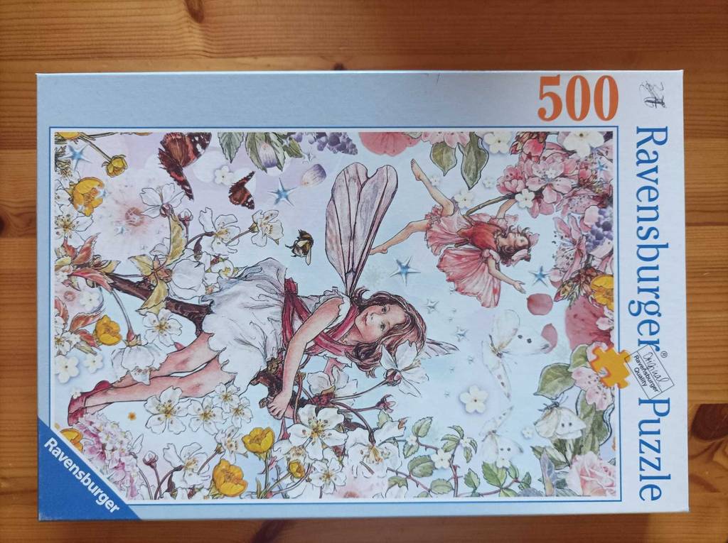Puzzle-Test: Ein 500-teiliges Feenmotiv liegt in Verpackung auf einer Holzfläche.