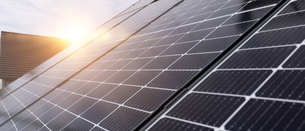 Einfamilienhaus mit Photovoltaikanlage auf dem Dach. Im Hintergrund geht die Sonne unter.