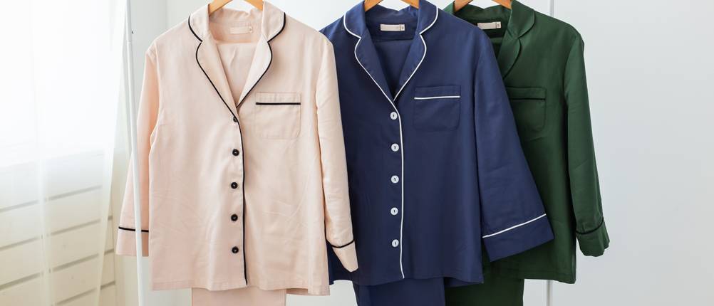 Pyjama-Damen-Test: Drei unterschiedlich farbige Pyjamas für Frauen hängen nebeneinander auf einer Kleiderstange.