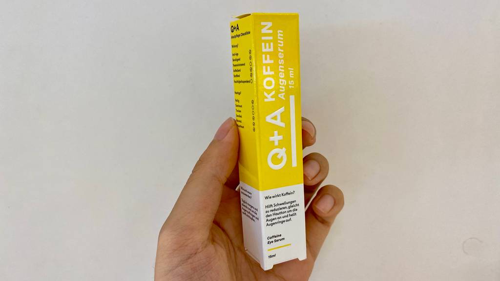 Im Test: Hand hält eine Packung Q+A Koffein Augenserum vor weißem Hintergrund.