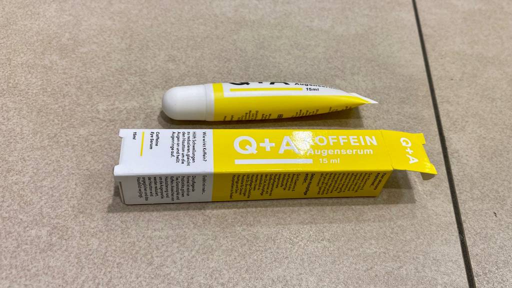 Im Test: eine Tube Q + A Koffein Augenserum liegt neben dem Verpackungskarton auf hellem Untergrund.