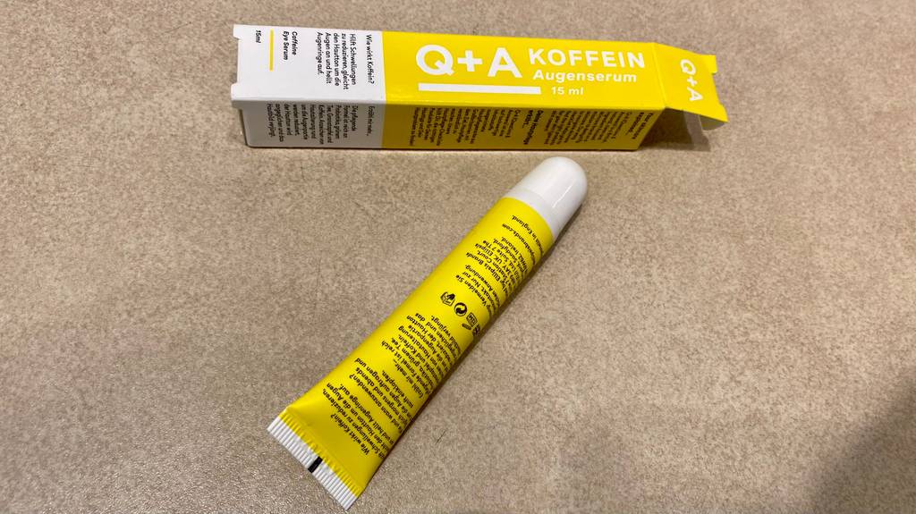 Im Test: eine Tube Q+A Koffein Augenserum liegt mit der Rückseite nach oben schräg vor dem Verpackungskarton.