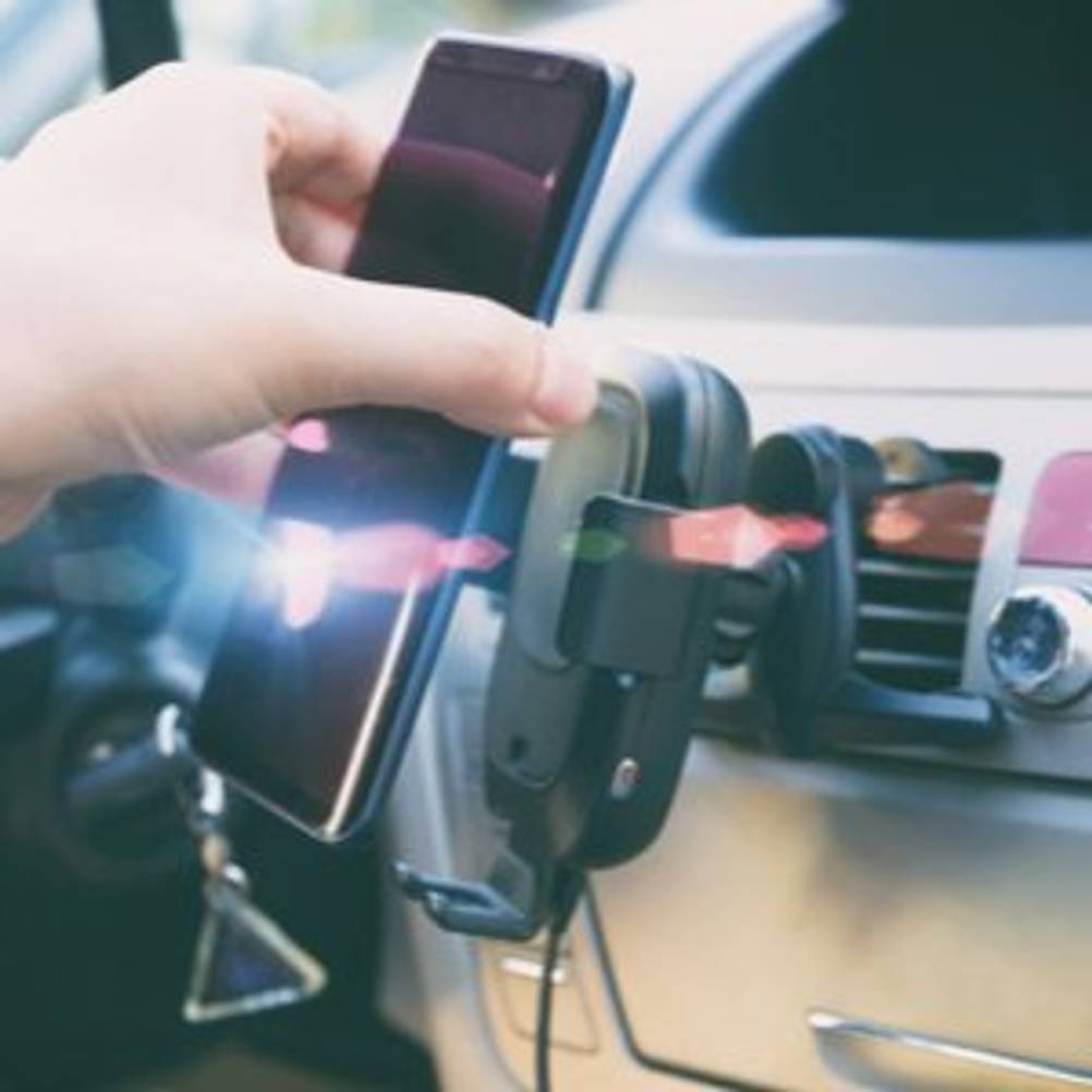 Autofahrer, der Smartphone aus seinem Qi-Ladegerät im Auto entnimmt
