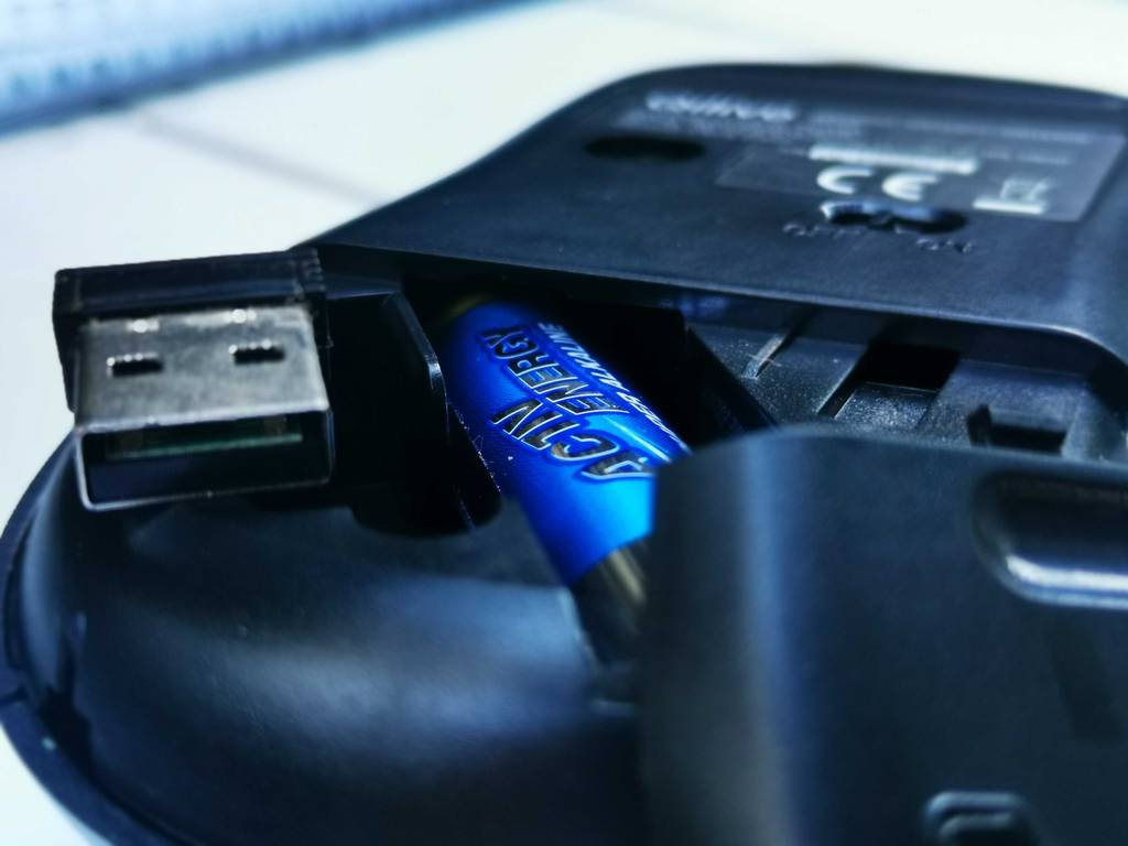 Im Test: Die Silent Mouse liegt mit Blick auf die im Inneren steckende Batterie und dem USB-Stecker auf einer weißen Oberfläche.