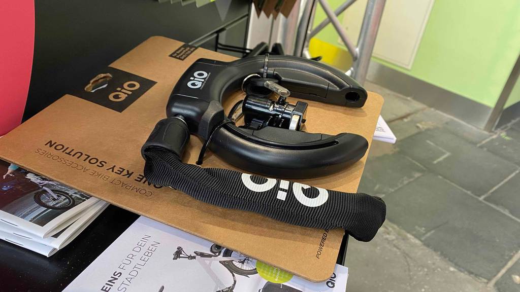 Ein schwarzes Fahrrad-Rahmenschloss mit Kette im Test liegt inklusive Zubehör und Verkaufspappe auf einem Ausstellungstisch.