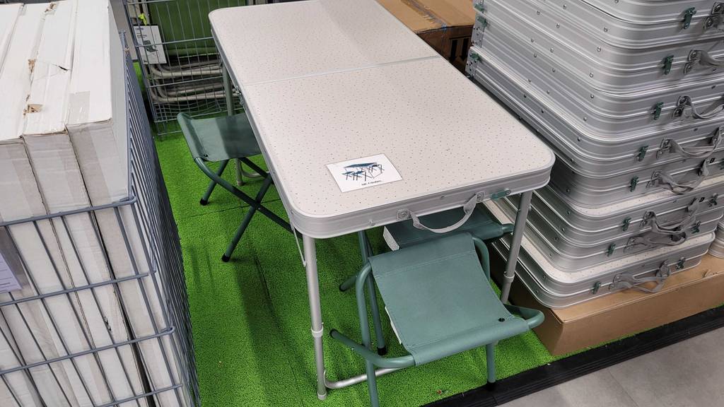 Ansicht von oben auf drei grüne Klapphocker und einen Campingtisch neben silberfarbenen Koffern, die dieses getestete Campingtisch-Set enthalten.
