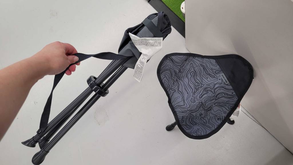 Im Test: Eine Hand hält einen zusammengeklappten Campinghocker über einem aufgestellten.