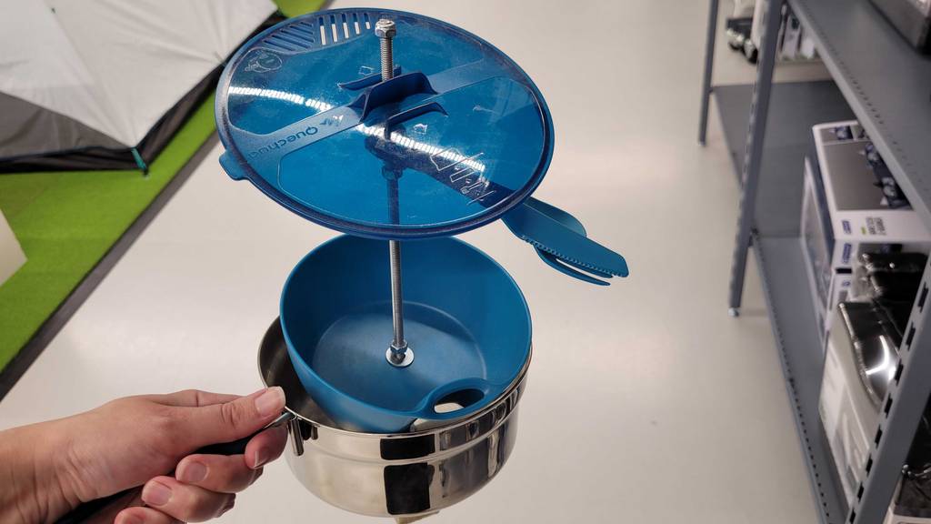 Im Test: Eine Hand hält ein zusammengestecktes Campinggeschirr mit Topf, Schale, Besteck und Deckel.