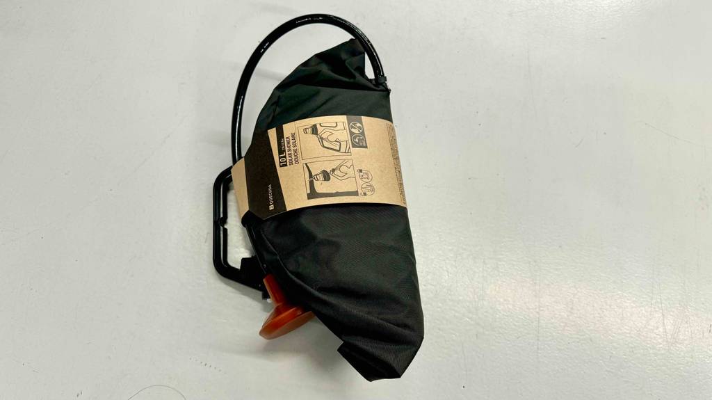 Eine Campingdusche liegt zum Testen mit Kartonbanderole auf einer weißen Fläche.