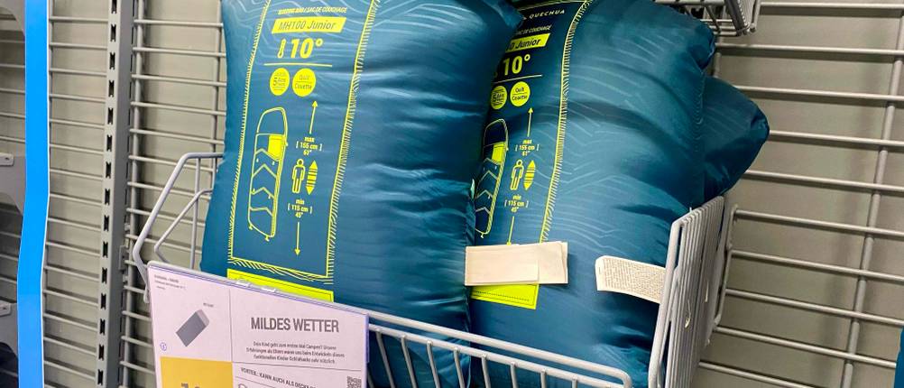 Kinderschlafsack-Test: Mehrere originalverpackte Produkte in einem Verkaufsregal mit Preisangabe.