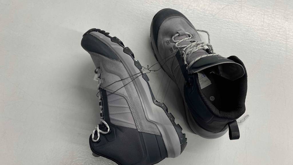 Im Test: ein Paar Bergschuhe für Herren in Grau/Schwarz auf weißem Untergrund, ein Schuh liegt seitlich.