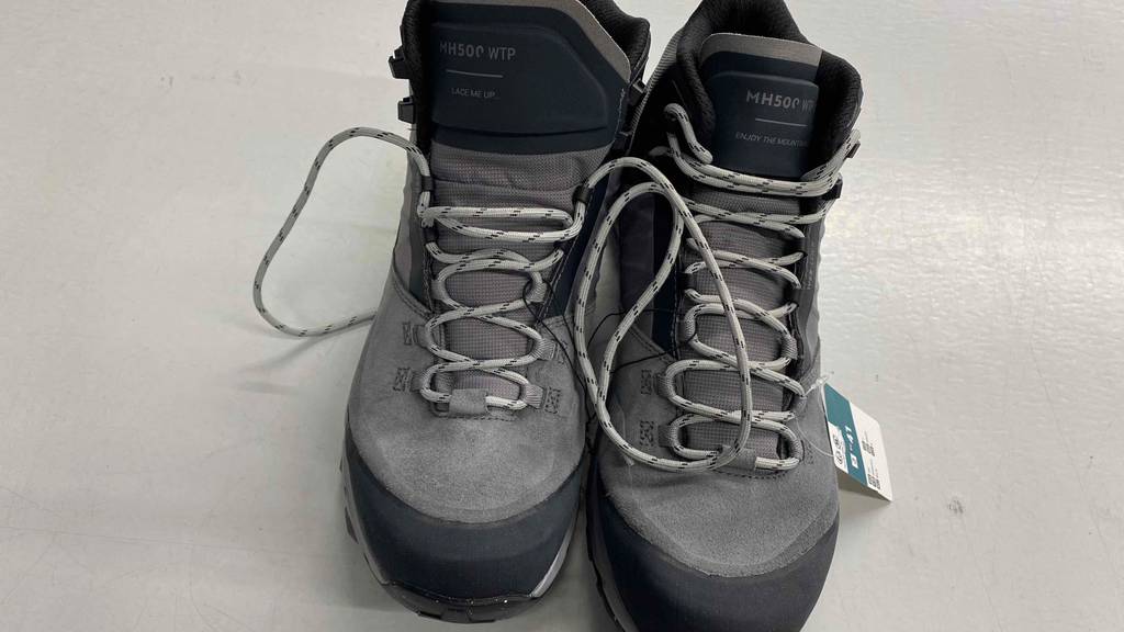 Ein Paar getestete Herren-Bergschuhe mit offenen Schnürsenkeln steht auf weißem Untergrund.