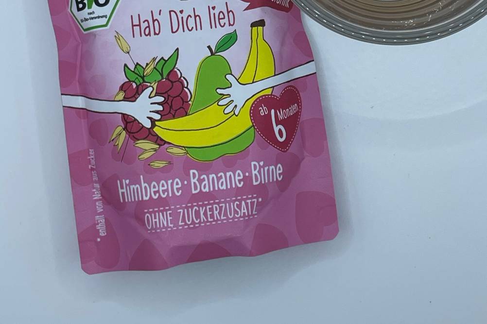 In einem Glas befinden sich getestete Frucht-Quetschies neben der Verpackung. 
