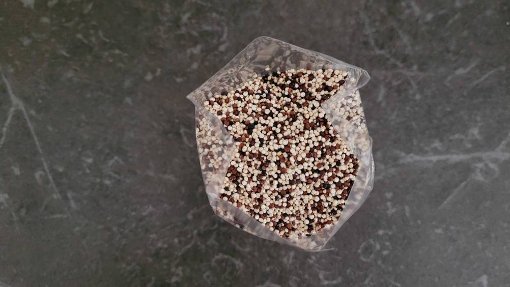 Blick von oben in eine geöffnete Packung des getesteten Quinoas auf einer dunklen Fläche.