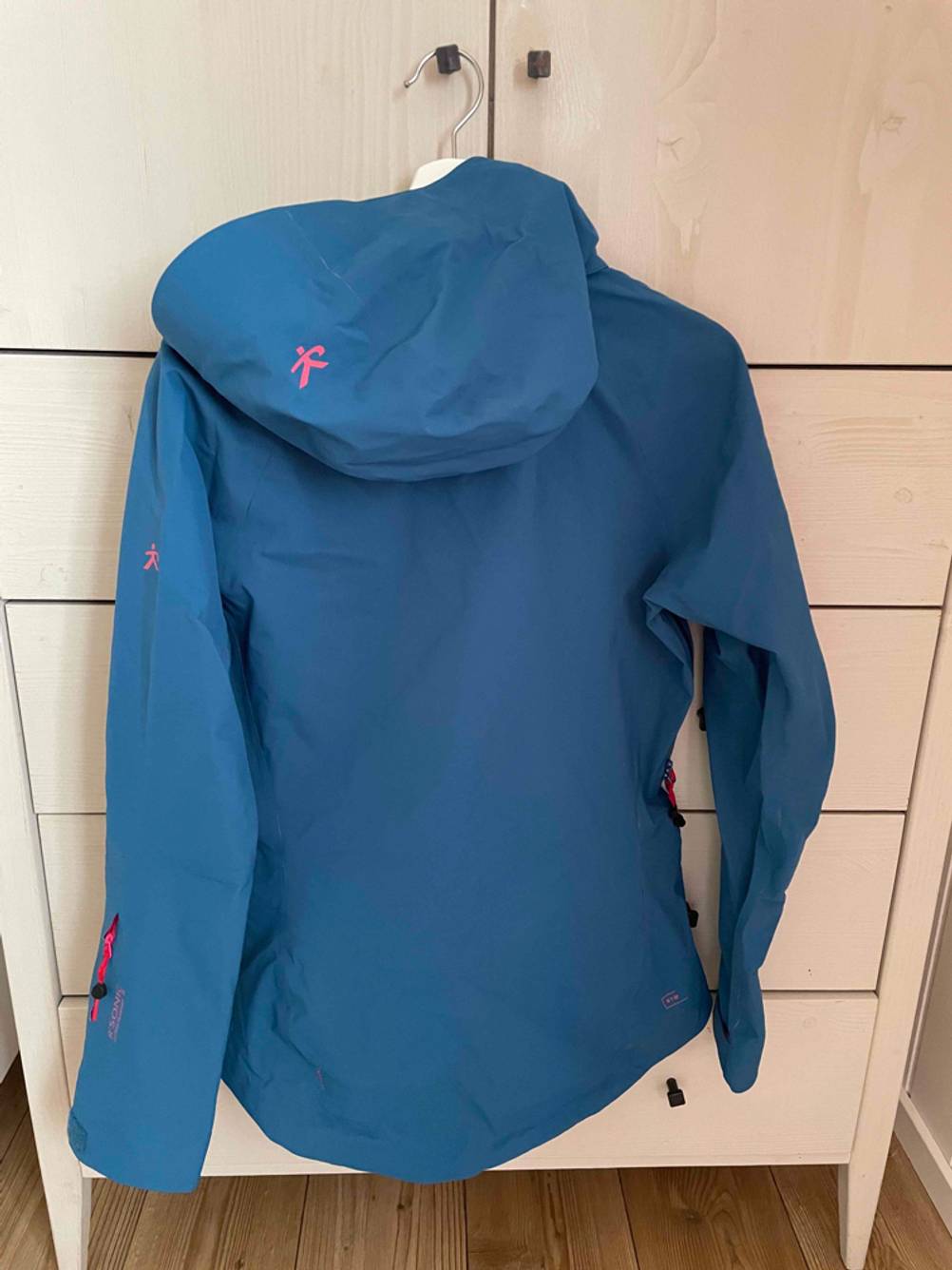 Hardshelljacken im Test: eine Jacke hängt mit der Rückseite und Kapuze nach vorn an einer weißen Kommode.