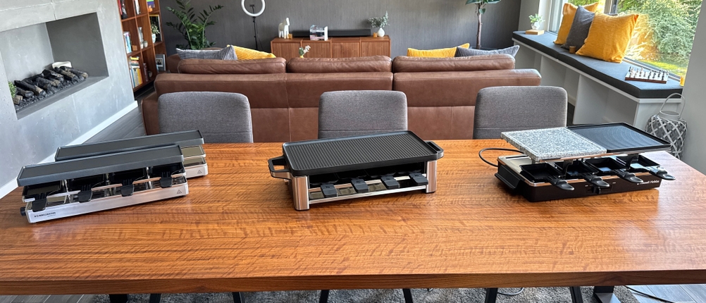 Drei Raclettes stehen nebeneinander auf einem Holztisch.