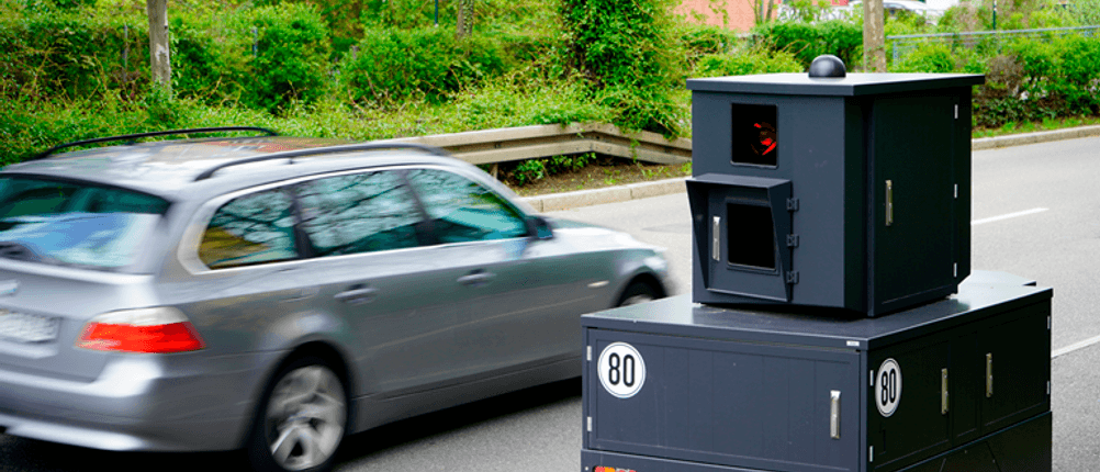 Radarwarner im Test: Ein Blitzer steht neben einer Straße, ein Auto fährt vorbei.