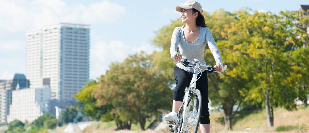 3/4-Radhosen-Damen-Test: Frau sitzt halb auf dem Fahrrad und blickt in die Weite; im Hintergrund ist ein Hochhaus zu sehen.