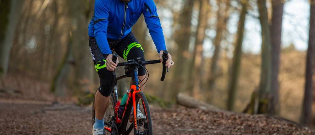 3/4-Radhosen-Herren-Test: Ein Mann in 3/4-Radhose fährt durch den Wald. Die Hose ist schwarz und hat gelb leuchtende Streifen.