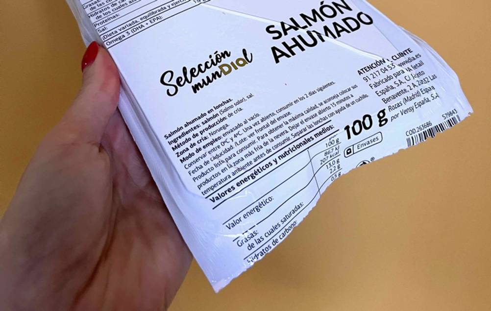 Räucherlachs getestet: Nahaufnahme der Rückseite einer Packung von einer Hand vor eine gelbe Wand gehalten.