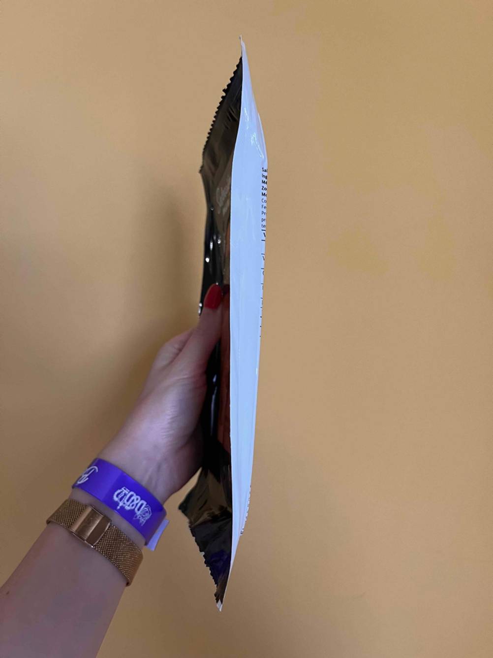 Seitenansicht einer Packung des getesteten Räucherlachses von einer Hand vor eine beige Wand gehalten.