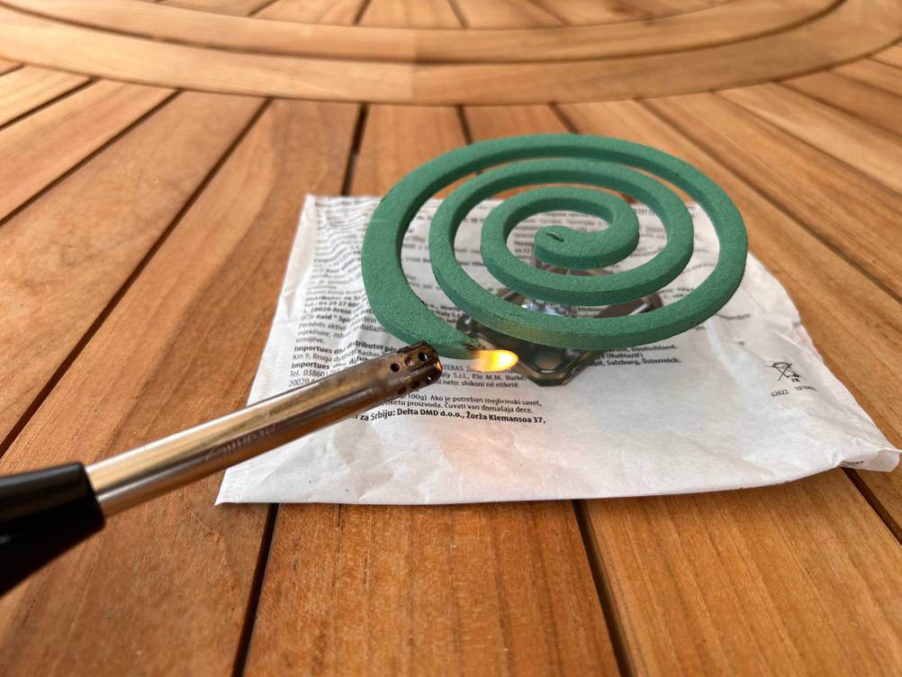 Im Test: Eine Mückenspirale auf einem Holztisch die von einem Feuerzeug angezündet wird.