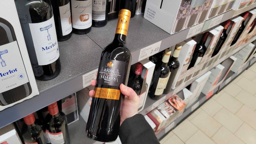 Eine Hand hält eine Flasche mit Rioja-Wein im Test vor einem Verkaufsregal.