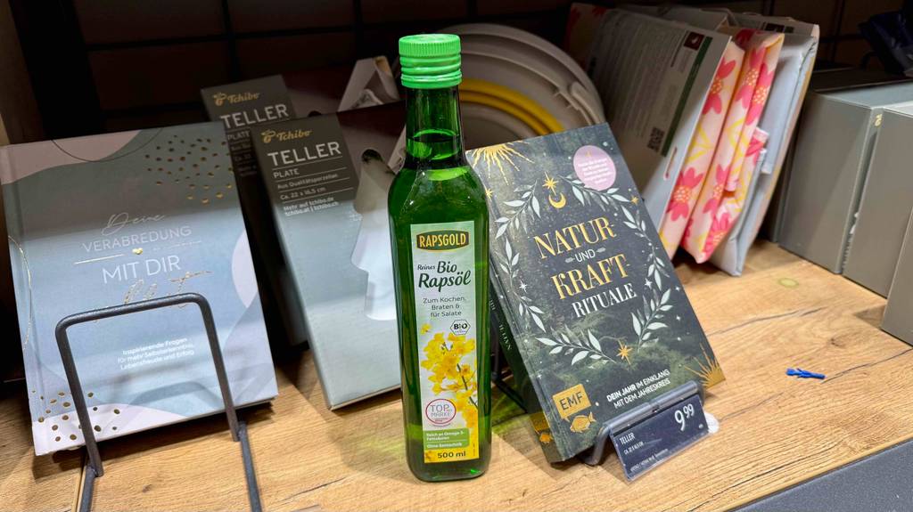 Eine Flasche Bio-Rapsöl steht zum Testen vor verpackten Tellern in einem Holzregal.
