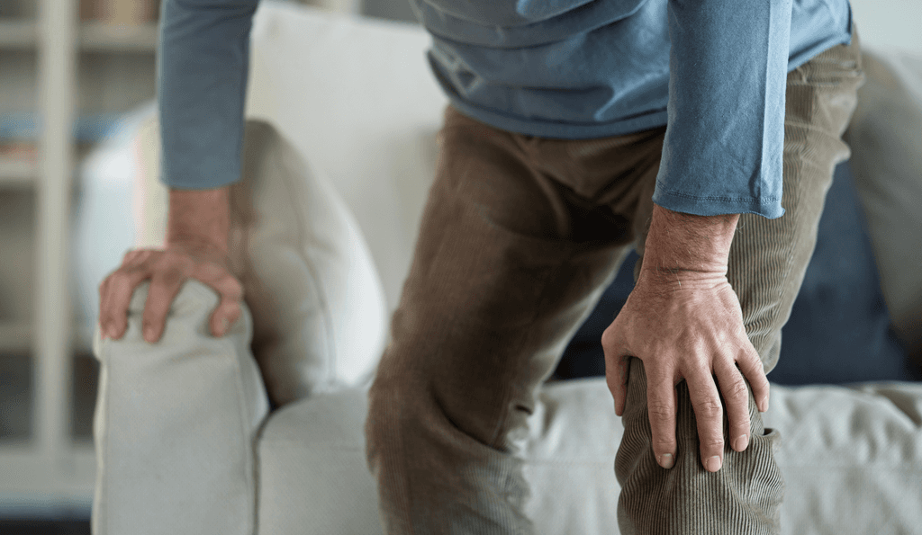 Rapssamen-Test: Ein alter Mann steht von der Couch auf und fasst sich an sein schmerzendes Knie. 